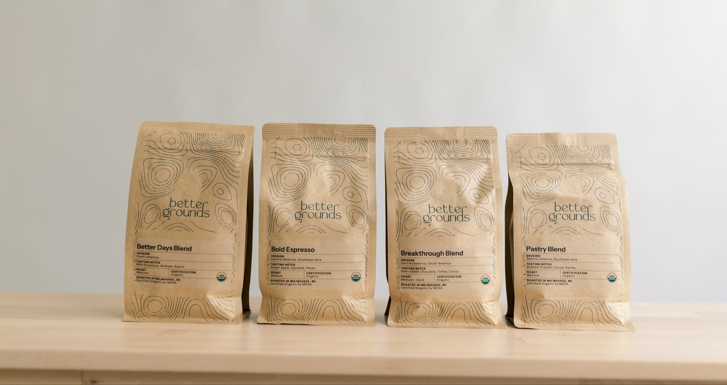 Four packages of 'Better Grounds' coffee on a wooden surface with a light gray background